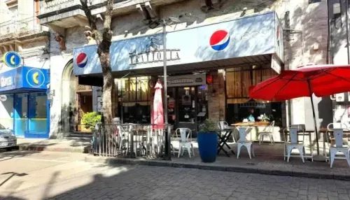 Frente del local con sombrillas rojas y mesas en la vereda